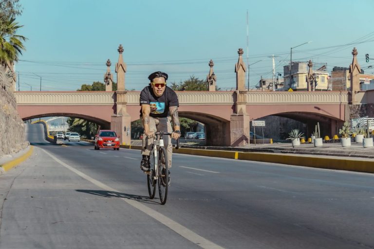 Ciclista urbano rodando por una avenida de León Guanajuato con un puente de arcos al fondo