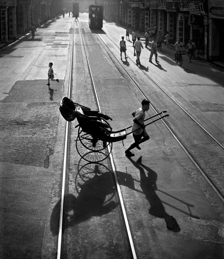 Fotografía de calle Different Directions de Fan Ho, 1958: siluetas y sombras a contraluz sobre vías de tranvía